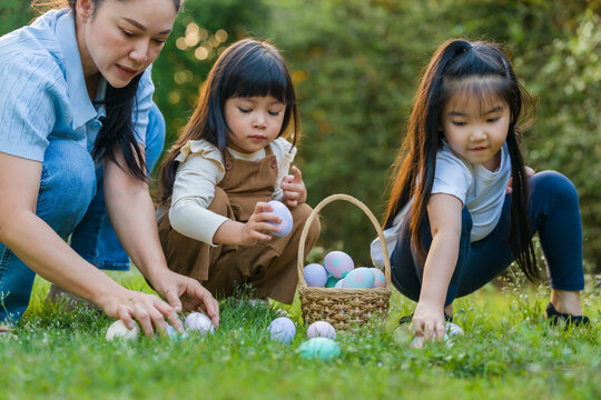 mother and her two daughters playing and hunting for Easter eggs into a basket on green grass in garden