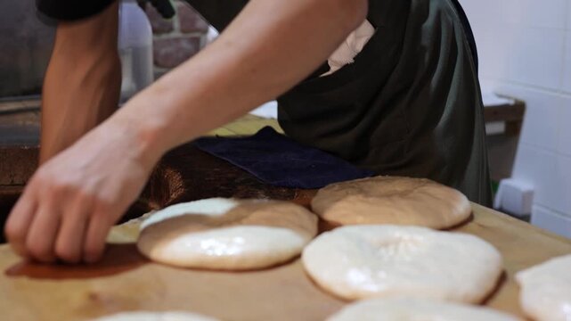 Man baker preparing flatbread dough on a wooden board next to a traditional tandoor oven for baking.