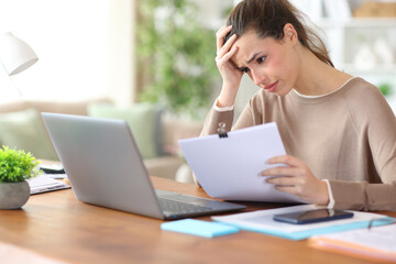 Worried freelance worker holding document checking laptop