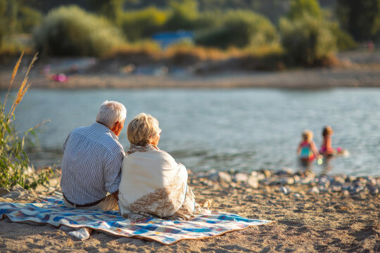 senior couple sitting on blanket watching grandchildren play near water, joyful family retirement scene, sunny beach day, candid emotional moment, professional lifestyle photography