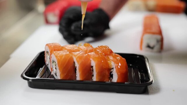Chef drizzling savory sauce over fresh salmon sushi rolls.