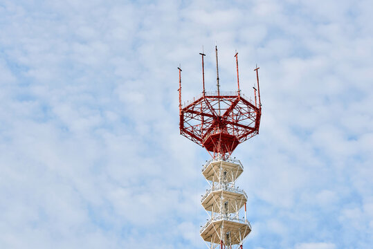 Tall telecommunication tower, red steel lattice antenna array and white octagonal platforms stands against bright blue sky. Industrial communication infrastructure, telecommunication antenna system