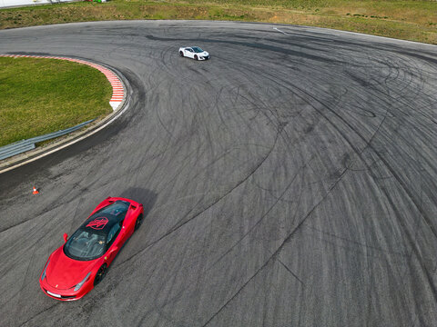 Aerial view of a red Ferrari 458 Italia and a white Honda NSX maneuvering on a curved asphalt track with tire marks, ODTJ Tomasz Kuchar, Czerwienica, Poland, Europe