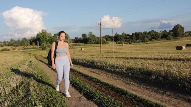 A woman in sportswear walks through a field in a village on a sunny summer day