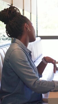 Vertical video: Speaking denim-shirt woman offering cup to friend in green top at cafe, phone near