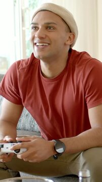 Vertical video: Reacting to game event, man in red tee pressing white controller on sofa with bowl