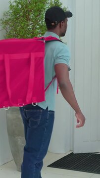 Vertical video: Stepping on mat driver wearing cap opening red thermal bag, handing pizzas to buyer