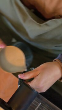Vertical video: Picking steam wand guard, barista in apron placing milk pitcher at cafe, frothing