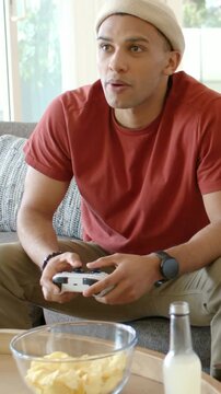 Vertical video: After game event man leaning gripping white controller on couch, second pad joining