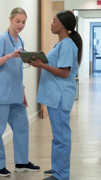 Vertical video: Checking nurses after hi, viewing tablet for chart in hall, stethoscope scrubs