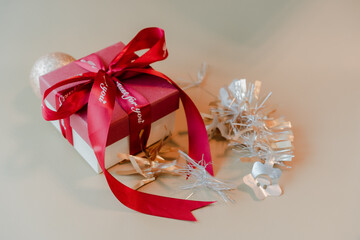 Christmas gift box with red ribbon and golden ornament on beige background, festive holiday still...