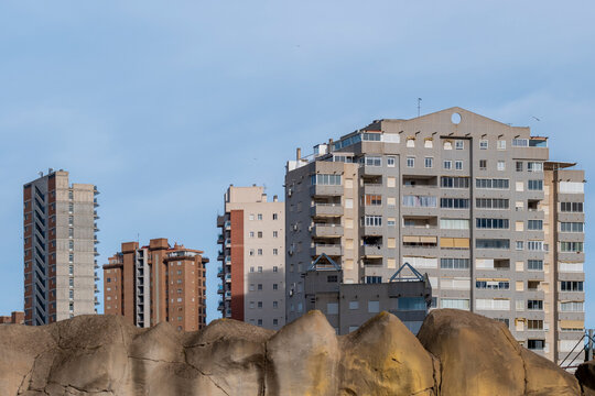 Tall apartments and buildings form a modern urban skyline in Benidorm Spain above rocks on a hillside under clear daylight and blue sky