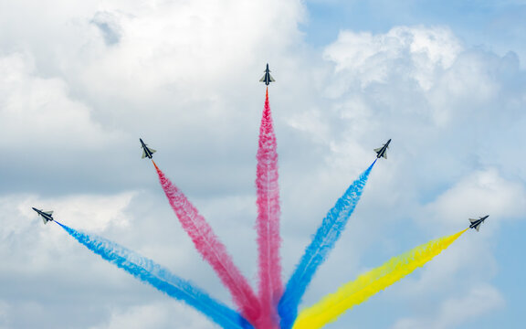 Aerial view of fighter jets soaring against a backdrop of fluffy white clouds, painting the sky with vibrant trails of red, blue, and yellow, Changi, Singapore.