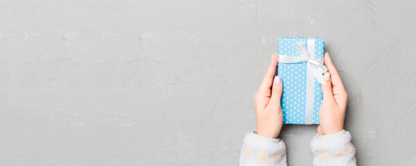Fototapeta premium Female hands holding present on grey cement background. Festive backdrop for Christmas holidays or other holiday . Flat lay style top view with copy space