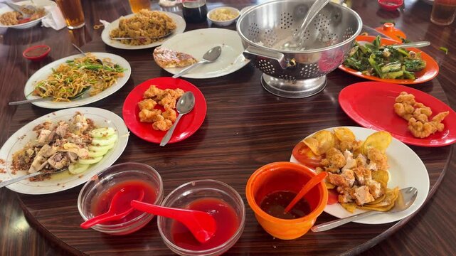 Chinese restaurant table scene of rice, chow mein fried noodles,egg foo young, fried shrimp or prawn, Stir-fried Chinese Greens and steamed chicken with fried garlic  on a rotating wooden table.