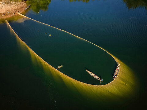 Aerial view of fishing nets cast in the dark, still waters, with boats poised at the edge, creating a captivating contrast of light and shadow, Kolkata, West Bengal, India.
