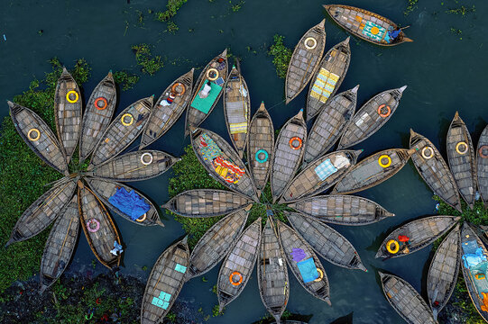 Aerial view of boats clustered in a flower-like pattern, their weathered wood contrasting with pops of colorful goods and life preservers, Kolkata, West Bengal, India.