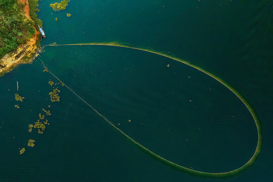 Aerial view of a large fishing net cast in the tranquil waters, forming a striking oval shape against the deep blue, Kolkata, West Bengal, India.
