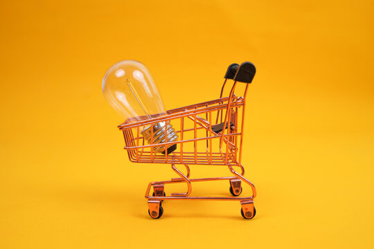 Studio Shot Of Miniature Copper Shopping Cart Carrying Clear Glass Light Bulb