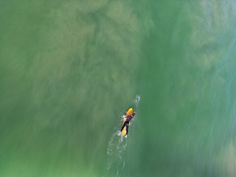 Aerial view of a lone surfer gliding across the shimmering turquoise waters, a dance of solitude and nature's embrace, Barbate, Andalusia, Spain.