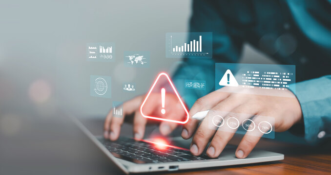 Hands typing on laptop with glowing warning alert and virtual data dashboard interface. Concept of cybersecurity risk, system error detection, data protection, online security monitoring technology