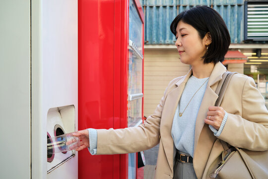 Woman recycling plastic bottle at vending machine outdoors