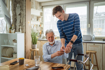 Fototapeta premium Young man assisting senior at home with health monitor