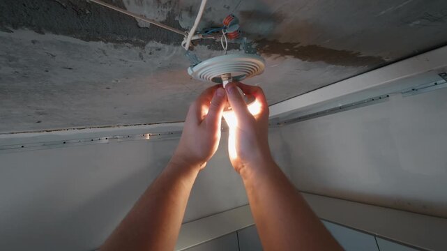 Hands installing ceiling light bulb into socket during repair