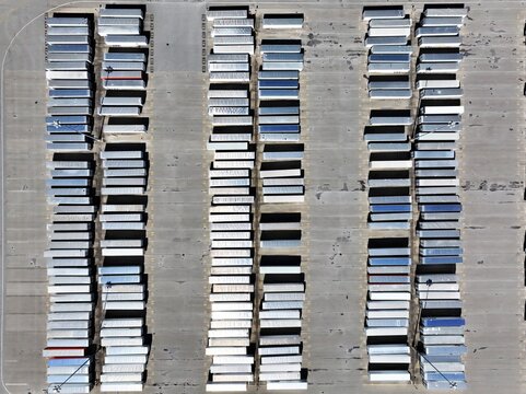 Aerial view of rows of shipping containers casting long shadows on the concrete expanse, creating a geometric dance of light and form, Greensburg, Indiana, United States.