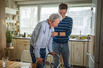 Young man assisting senior using walker at home