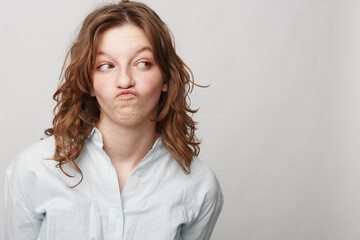 Young woman with curly hair wearing white shirt makes funny face looking sideways. Studio portrait...