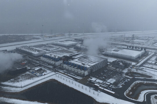 Aerial view of a large modern data center complex covered in snow, emitting steam from cooling units during winter, Eemshaven, Netherlands.