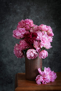 Pink peony bouquet in vase on wooden table in studio setting