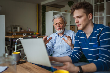 Fototapeta premium Young man teaching senior man using laptop at home