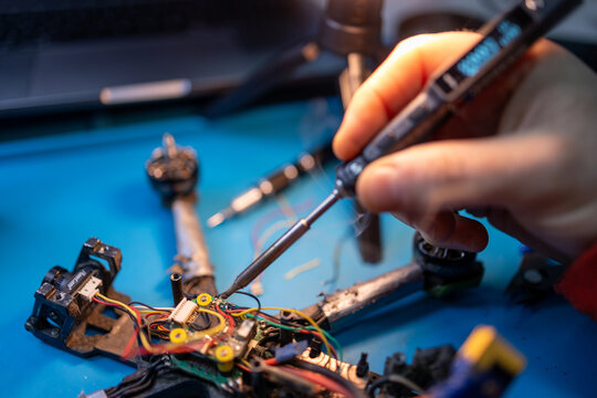 Technician soldering a 5-inch FPV drone on a workbench, with exposed electronics, wires, and repair tools.
