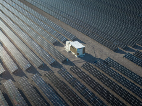 Aerial view of solar panels stretching across the arid landscape, punctuated by a lone white structure, creating a stark contrast of light and shadow, Searchlight, Nevada, United States.