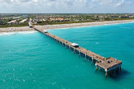 Aerial view of the Juno Beach Pier stretching out into the turquoise Atlantic waters, contrasting with the sandy beach and lush greenery, Juno Beach, Florida, United States.