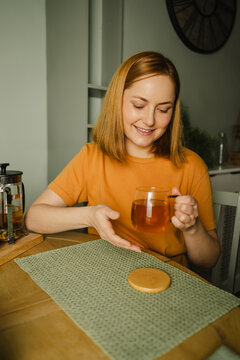 Smiling woman enjoying organic herbal tea at kitchen table