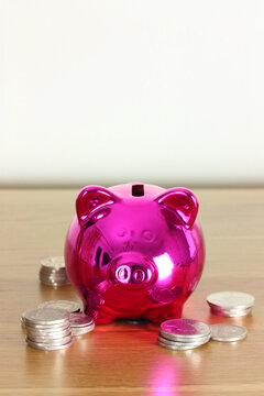 Pink piggy savings bank with coins on a desk