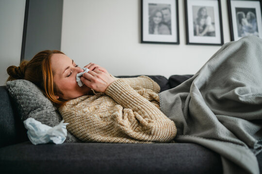 Person lying on sofa with flu and fever wrapped in blanket indoors