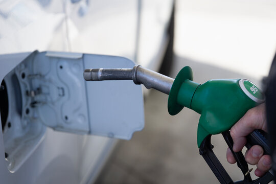 man refilling car with e20 biofuel and 95 octane gasoline at gas station, close up of hand holding green fuel nozzle into white vehicle, concept of energy transition, oil industry, fuel economy