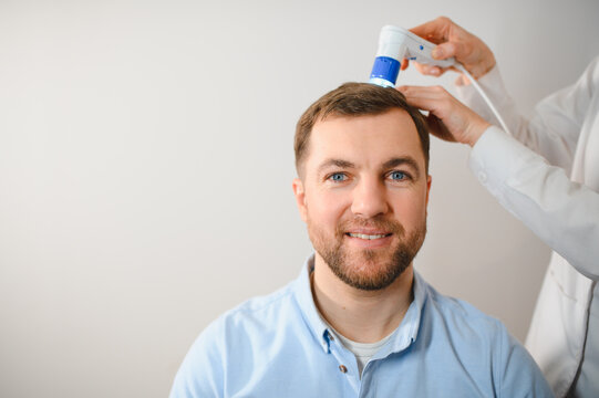 A young man is examined with a trichoscope the condition of the scalp and hair follicles