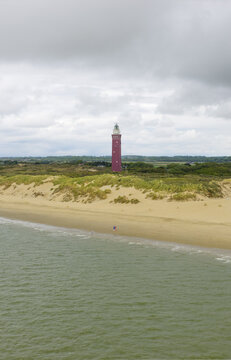 Aerial view of the Westhoofd Lighthouse standing tall against the muted greens and sandy tans of the Ouddorp coastline, Ouddorp, Zuid-Holland, Netherlands.