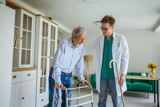 Healthcare worker assisting senior man with walking frame