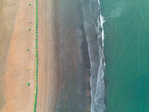 Aerial view of green sunshades lining the sandy beach where the ocean's dark waves meet the shore, Cox's Bazar, Chittagong Division, Bangladesh.