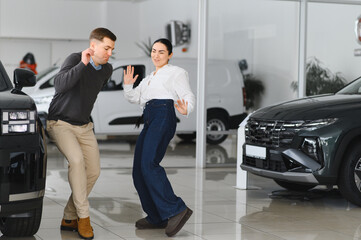 Cheerful couple young woman and man dancing after buying new car in showroom