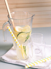 Fototapeta premium a pitcher and glasses with lemonade and lime and lemon slices on a beige linen tablecloth in natural light