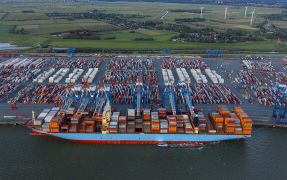 Aerial view of a massive container ship dwarfed by towering gantry cranes amidst a sea of colorful containers in the port, Bremerhaven, Bremen, Germany.