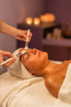 Young woman receiving massage with brush and water in spa salon - Beautiful girl wearing towels lying on massage tables at spa resort - Vertical photo