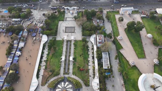 Aerial view of MGR Memorial complex along Marina Beach Road in Chennai, showcasing landscaped gardens, modern white memorial structures, palm-lined walkways, and busy traffic moving along the coast.